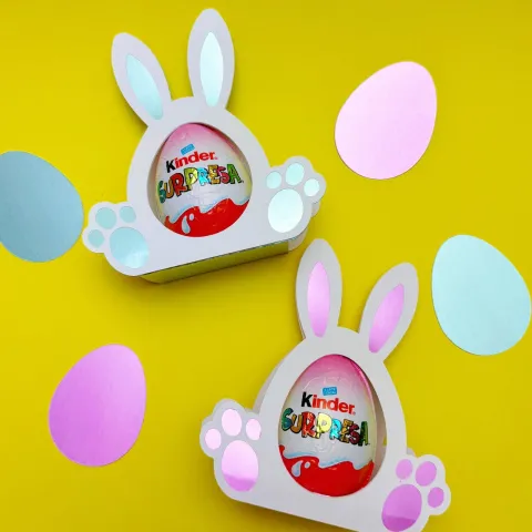 bunny-shaped candy egg holders made from cardstock holding a chocolate egg 