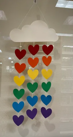 White cardstock cloud with three strands of rainbow hearts coming from the bottom of the cloud. 