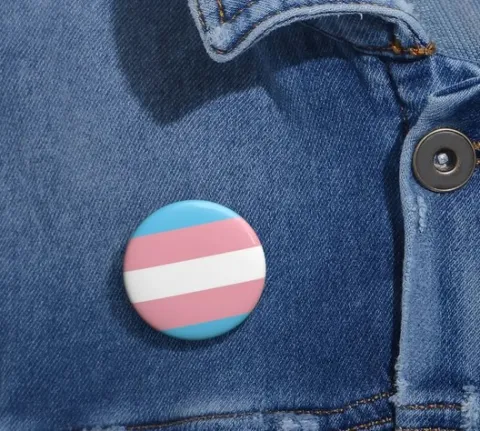 round pin with blue, pink, and white stripes on a denim jacket