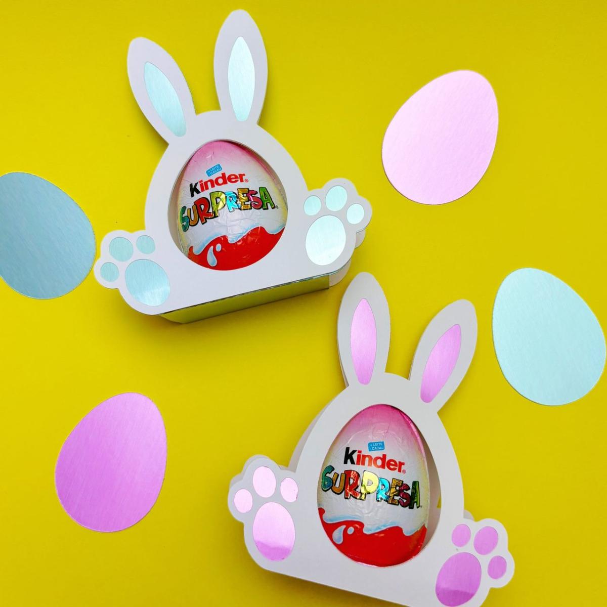 bunny-shaped candy egg holders made from cardstock holding a chocolate egg 