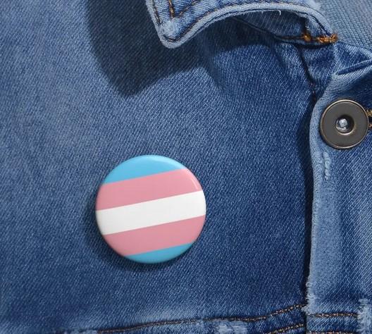 round pin with blue, pink, and white stripes on a denim jacket